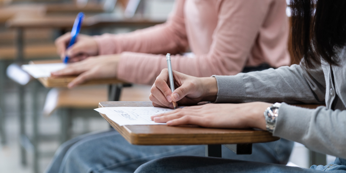 Students writing answers on an exam sheet in a classroom.