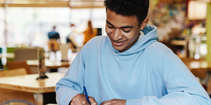 A cheerful student writing in a notebook while studying in a modern workspace.