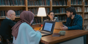 A group of university students studying together in a library, engaged in a discussion.