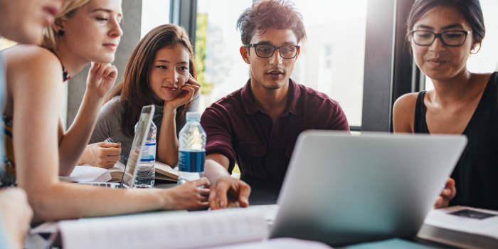 International students studying together around a laptop and books in a modern campus setting.